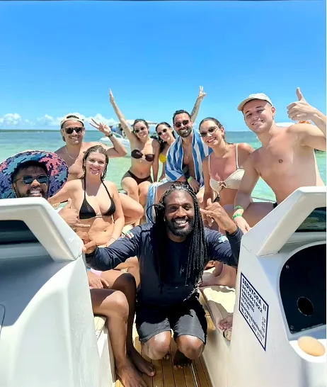 Djavan agachado com um grupo de clientes, mar azul turquesa ao fundo