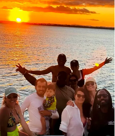 Grande grupo de clientes, com uma criança pequena, de braços erguidos contra o pôr do sol