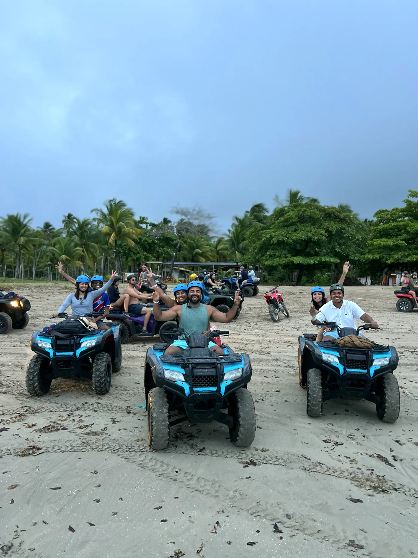 Grupo em quadriciclos azuis na praia, entre coqueiros, no passeio do Djavan