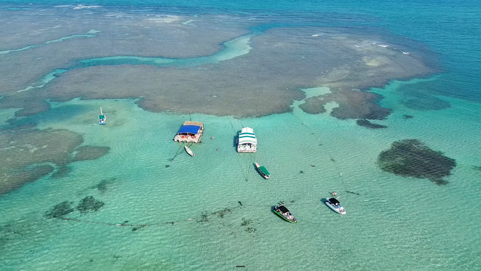 Vista aérea das piscinas naturais de Canavieiras, com bares flutuantes e lanchas ancoradas em água turquesa, parada do passeio Volta à Ilha